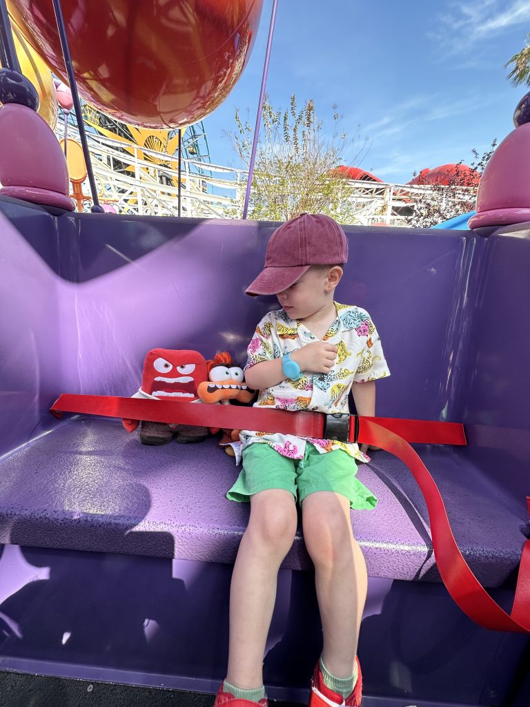 a toddler rides the inside out ride at disneyland with his anger toy sitting next to him