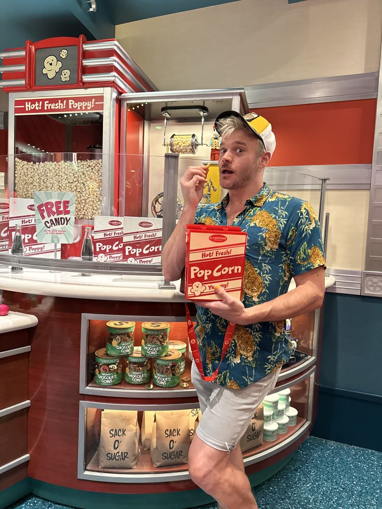 man takes a cheeky photo eating popcorn while standing infront of a disney popcorn stand